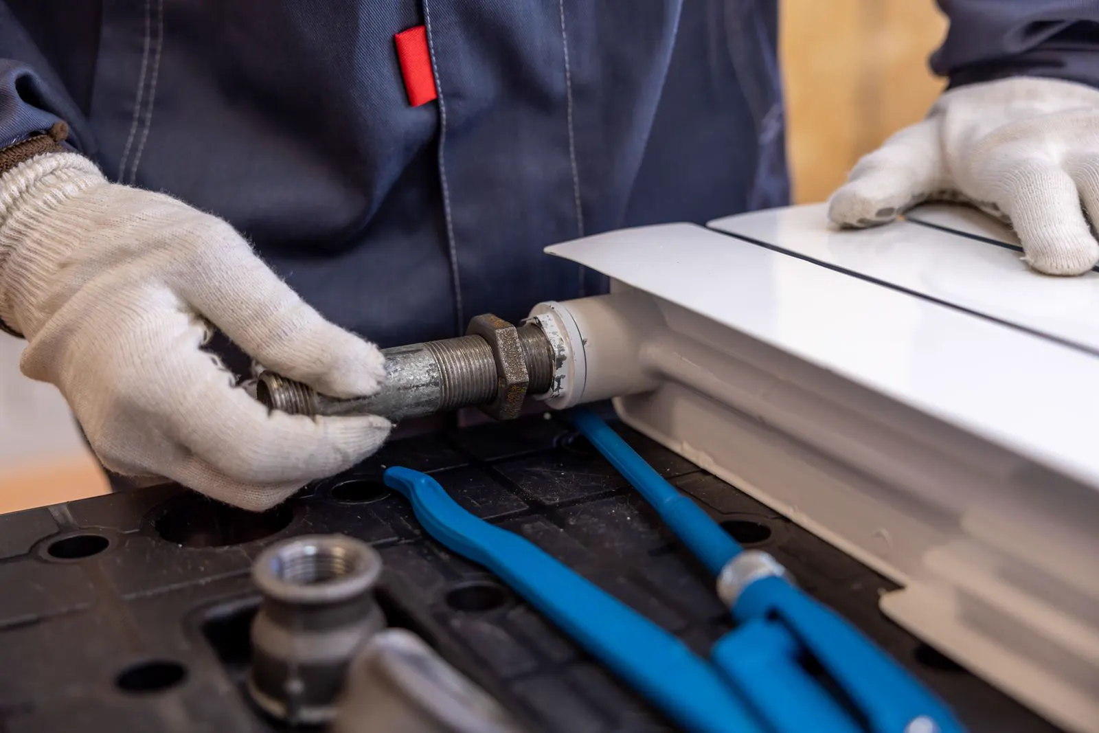 Plumber's gloved hands fitting a new pipe connection